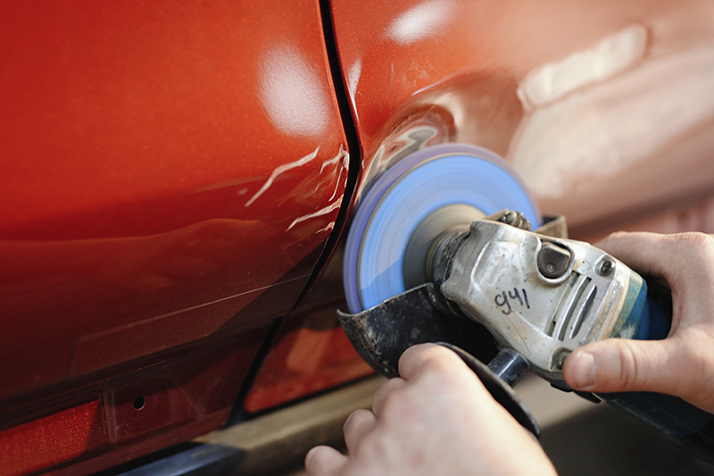 Auto technician repairing vehicle body damage with power tool